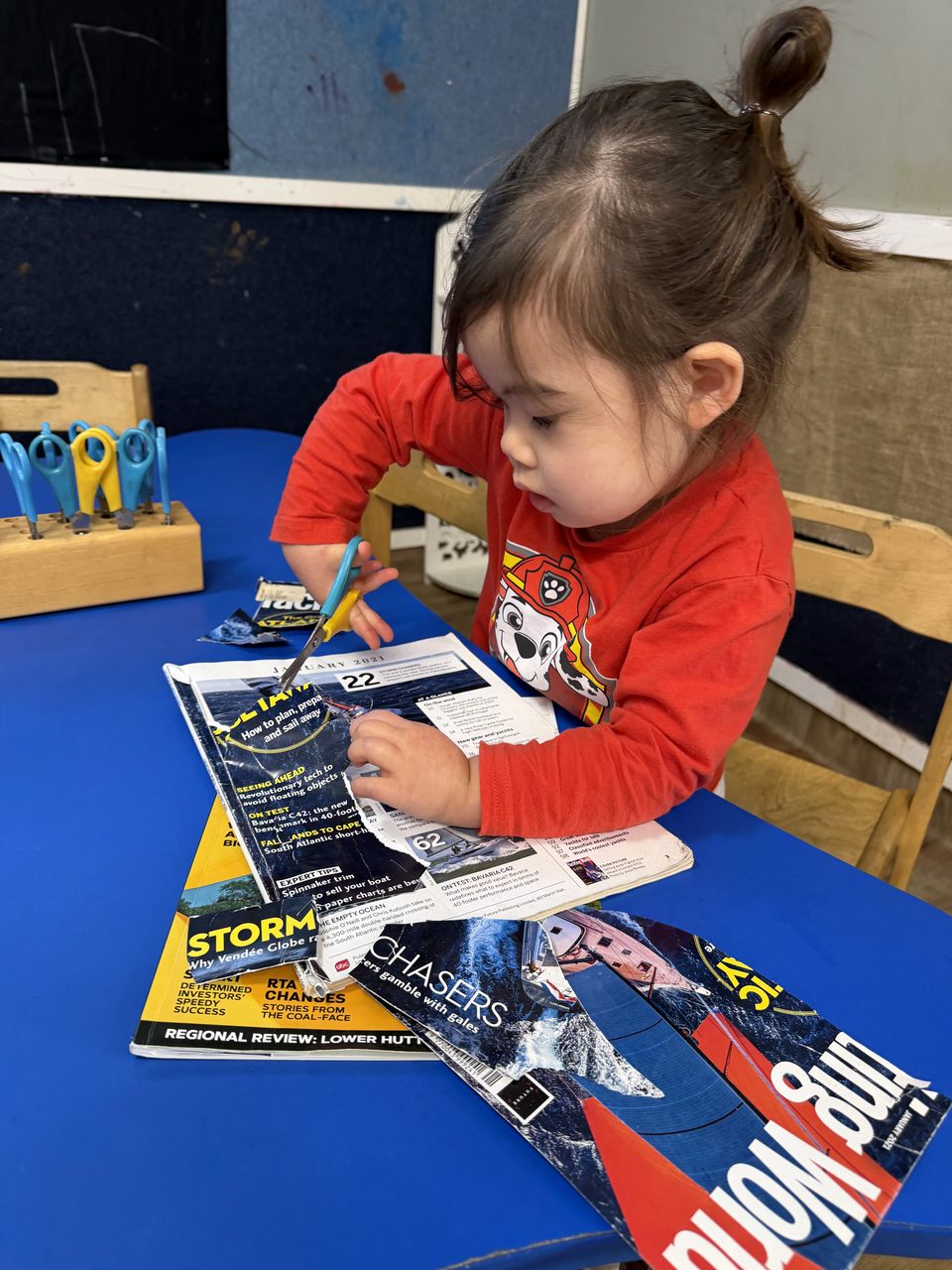A child concentrating while using scissors in a creative learning activity